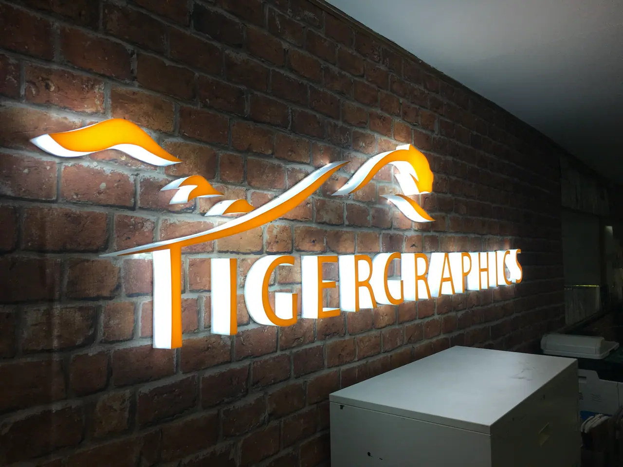 Illuminated Tigergraphics logo sign on a brick wall