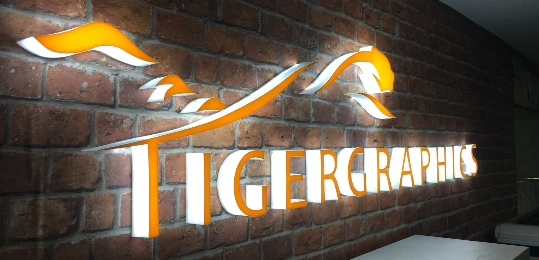 Illuminated Tigergraphics sign on a brick wall